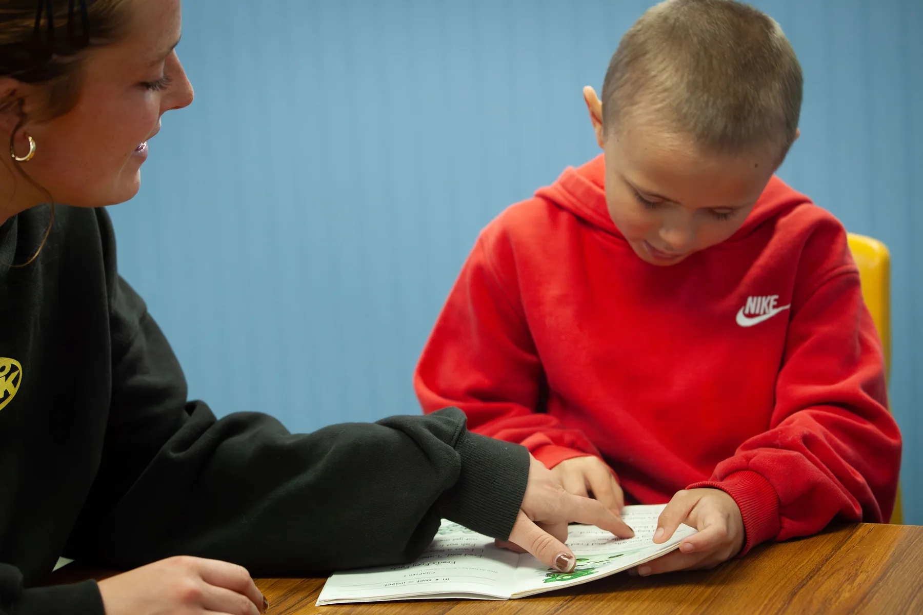 A ROW volunteer guiding a young reader in a red hoodie