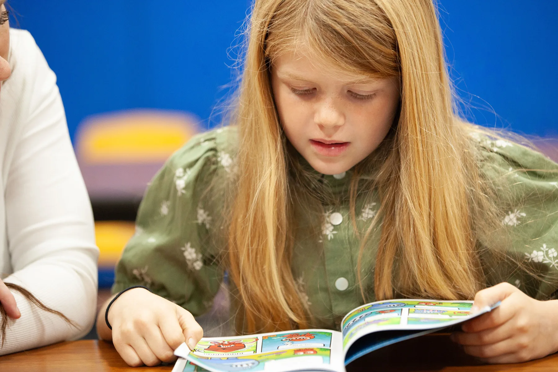 A student reading a colorful book with a volunteer