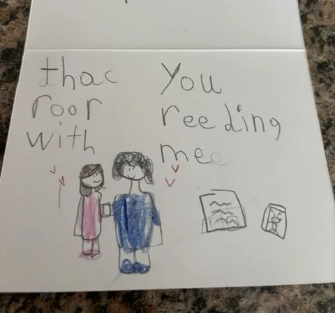 An open thank-you card with a child’s drawing of a student and ROW reader